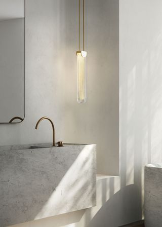 A bright bathroom with a hanging light near a limewashed wall. There are neutral and light tones used within the bathroom.