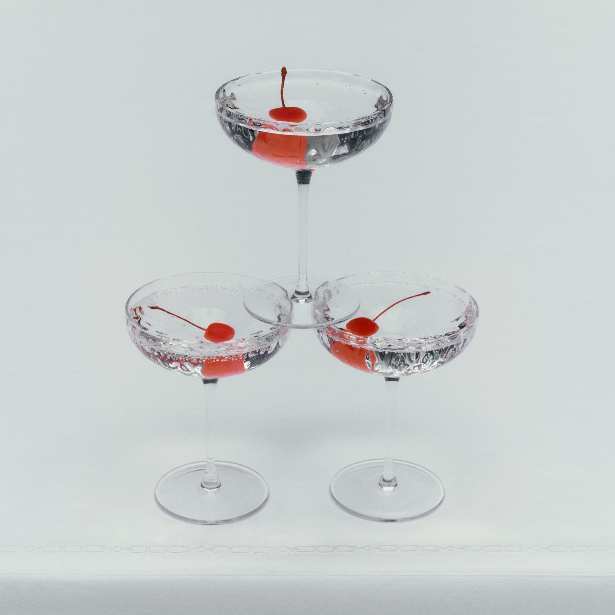 Three Aubrey Mouth-Blown Champagne Coupes stacked on top of each other filled with clear drink and cherries