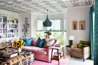 living room with pink sofa and teal curtains along with patterend ceiling and white bookshelves