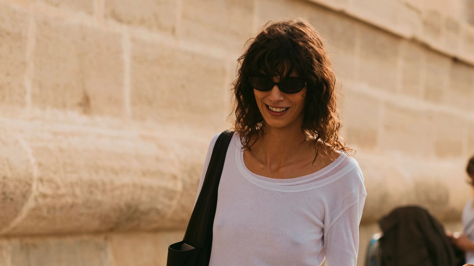 A woman wears a white shirt and black shoulder bag.