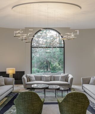 A large chandelier over a living room with tall ceilings and a large arched black doorway