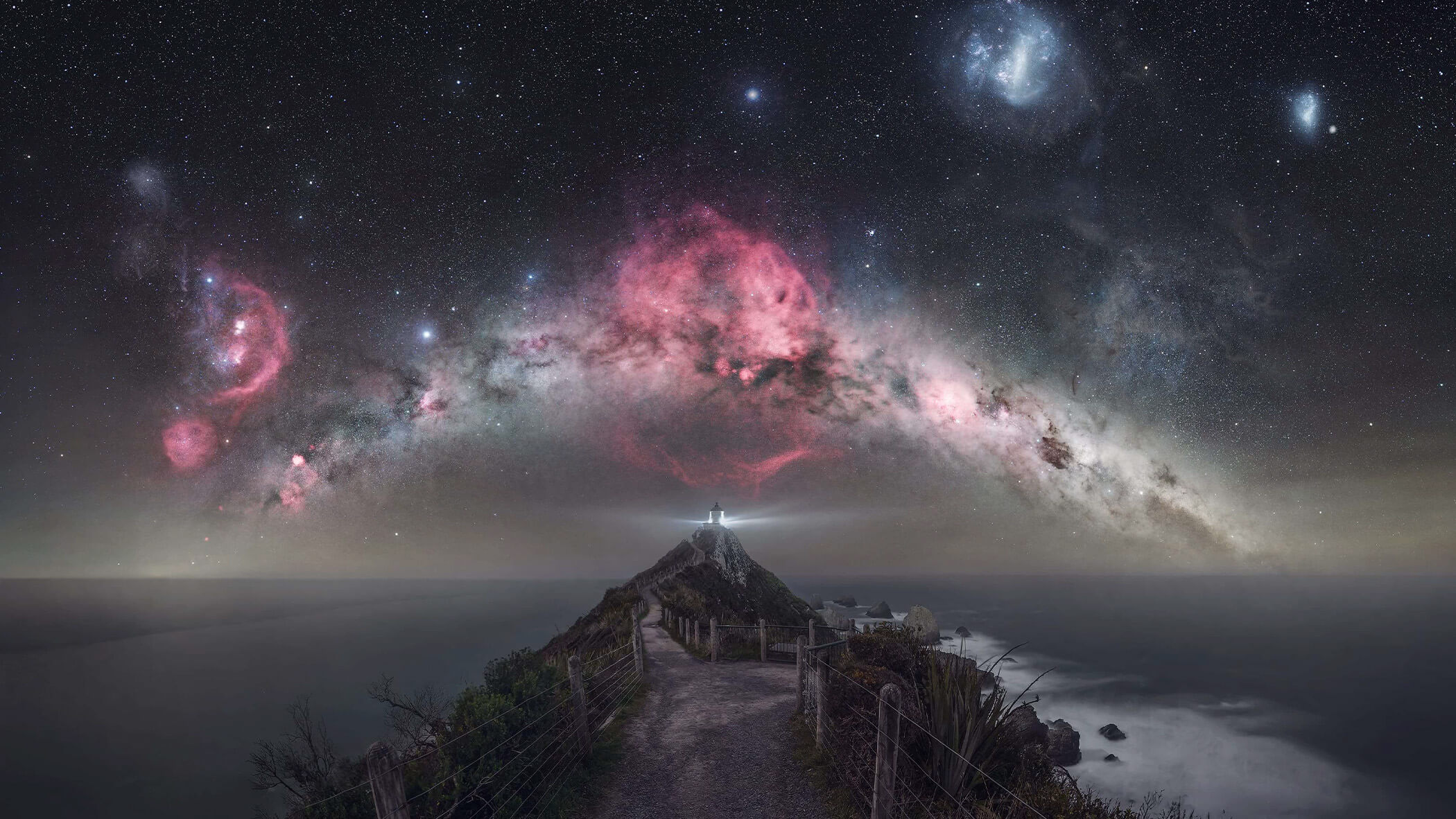A lighthouse beams below a Milky Way clad sky.