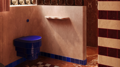 Image of a maximalist pink and red bathroom with electric blue accents. There is an electric blue toilet on a pink wall. The floors are a red and white checkerboard tile. There is a red marble shower with a glass brick divider.