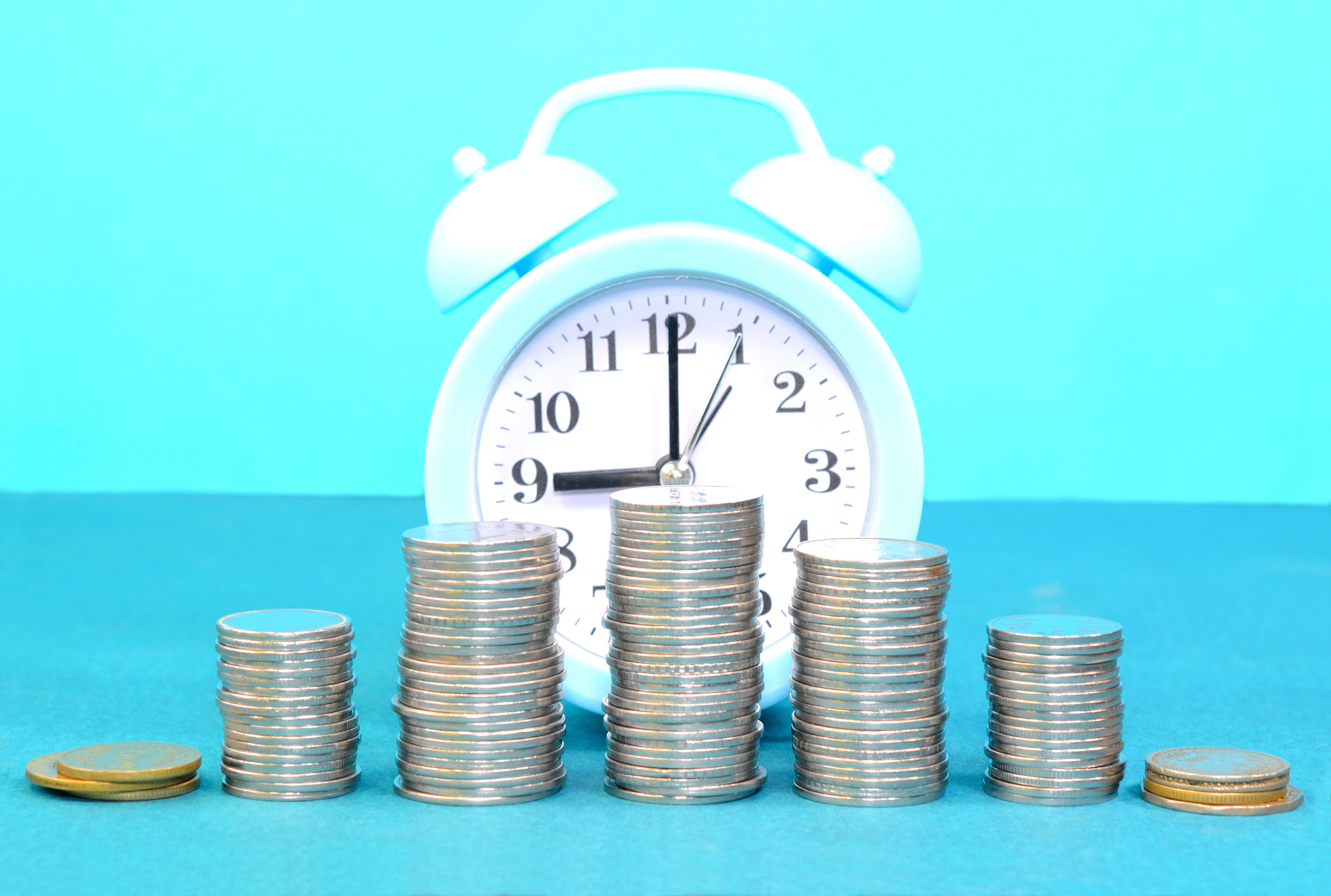 blue alarm clock with stacks of coins in the foreground