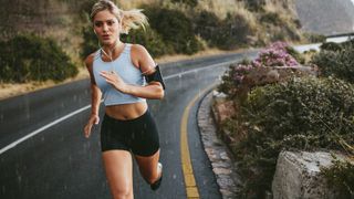 Woman in activewear running along a road with an arm band and headphones in