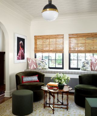 Sun room with green armchairs, striped windowseat, rattan blind, globe pendant and patterned rug