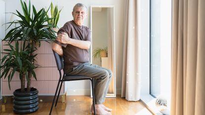 Man with white hair sits in chair and twists to one side