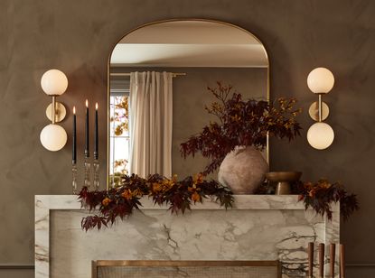 A marble fireplace decorated with a mirror, dried flowers and two wall lights