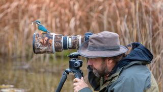 Man tacking pictures of birds surrounded by reeds and a bird on his camera