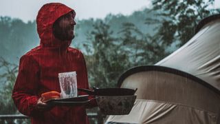 how to keep your tent clean while camping: man in the rain with dishes