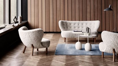 A curved off-white boucle lounge chair and sofa with white marble side tables in a wood panelled room