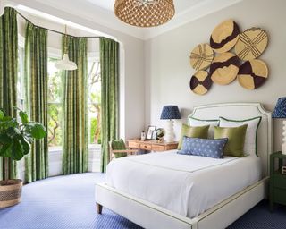 Modern bedroom with green curtains, blue carpet, large bed, decorative baskets on wall, pendant light