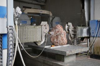 Large red stone with white speckles being cut by a machine to become a chair