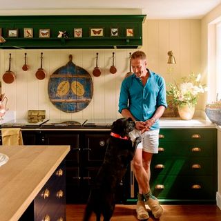 kitchen with green cabinet wooden counter and man standing with dog