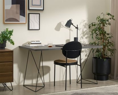 Made Solly Wide Desk with concrete-effect top and black legs, beside plant and with rattan chair