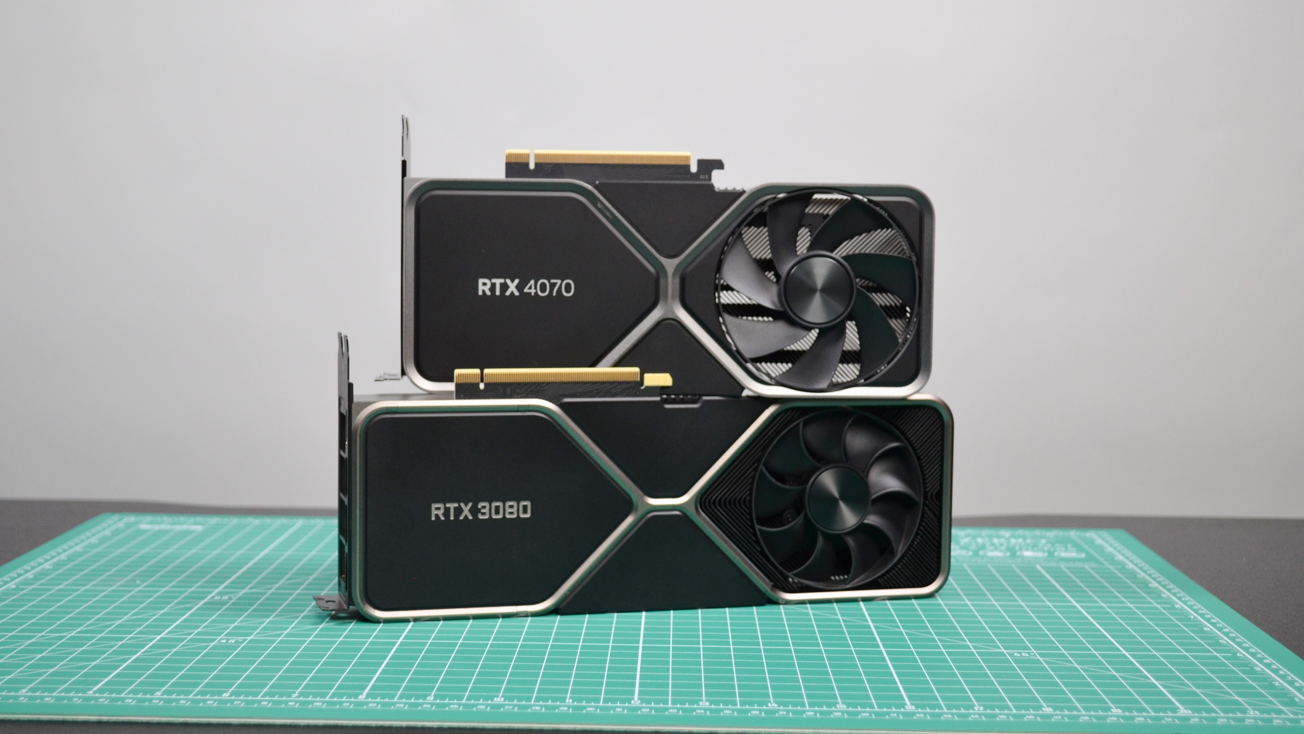 Die Nvidia RTX 4070 und RTX 3080 zusammen auf einer grünen Arbeitsfläche abgebildet.