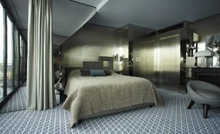 Grey green hotel room with patterned carpet, mirror wall and grey chair