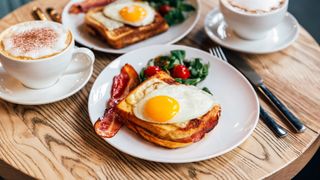 Fried eggs on bread with bacon and greens, breakfast table with coffees