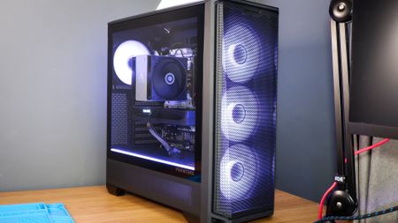 A gaming PC sat on a desk with purple RGB lighting on the fans and light bar enabled.