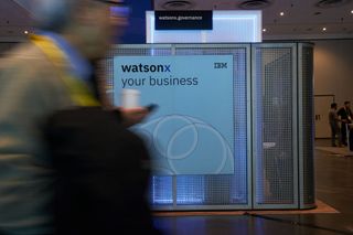 A sign at a conference showing the words IBM Watsonx, with a blurred man walking in the foreground