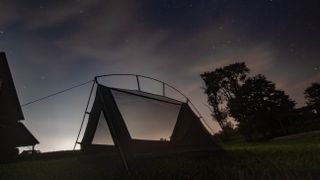 A triangular tent sits on some grass under the stars.