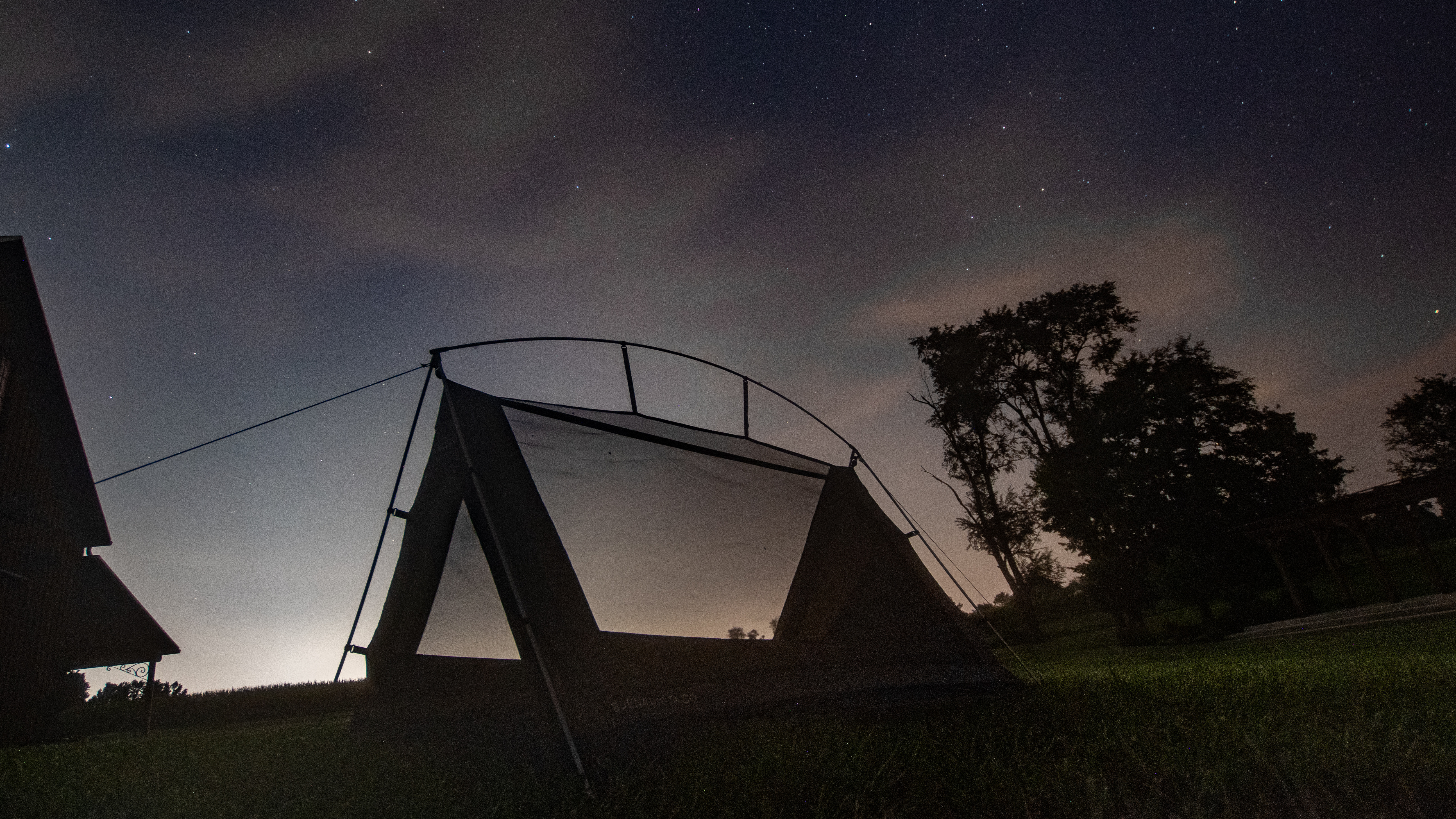A triangular tent sits on some grass under the stars.