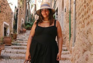 Woman wearing plus-size fashion dress black corset mini dress standing in European-style alleyway.