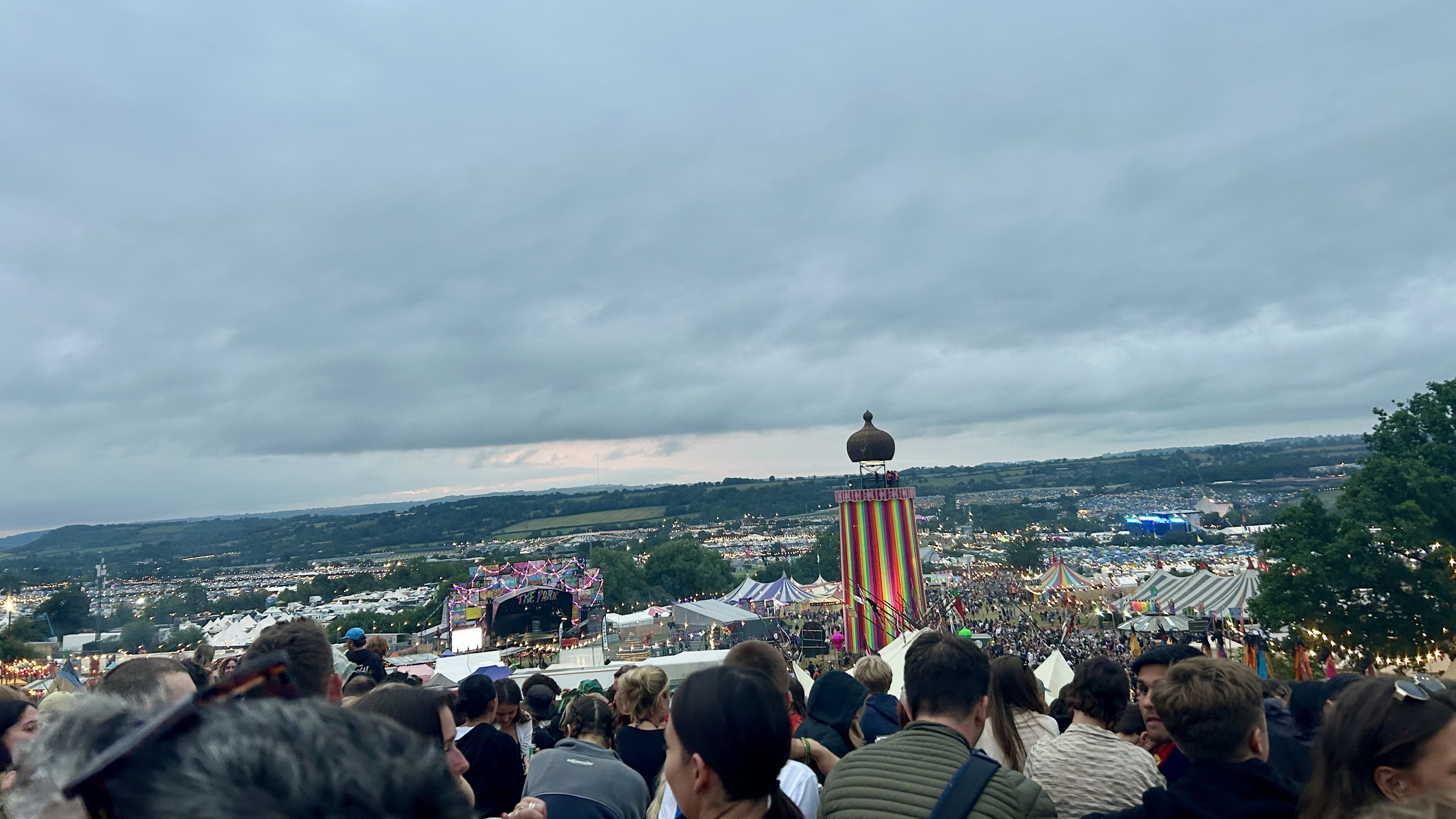 A photo of a large crowd at Glastonbury Festival with a lit-up ribbon tower