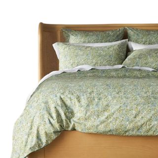A light green floral patterned duvet set with a duvet and four pillows, on a light wooden bed frame