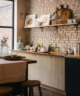 checklist for modern rustic style, modern rustic kitchen, pared back style, rough wood cabinetry, copper countertop, brass faucet, open shelving, open brick wall, table and stools, terracotta tiles