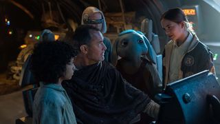 A group of kids and a blue alien gather around a man in a spaceship