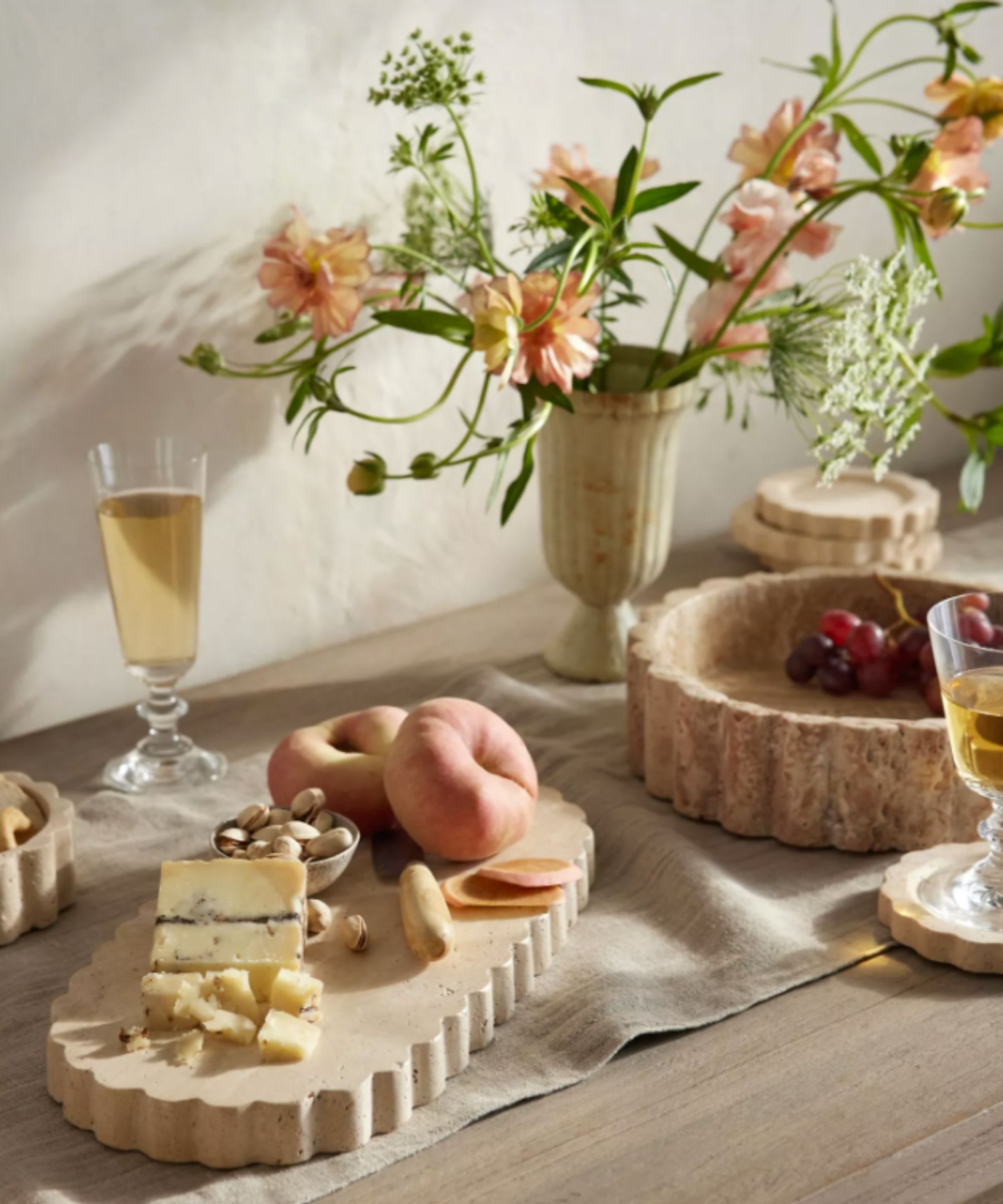 scalloped neutral serving platter and bowl with cheese, nuts and fruit and a vase of peach colored flowers