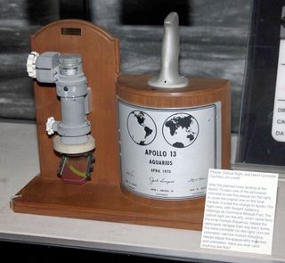 Apollo 13 lunar module crewman optical alignment sight (COAS), at left, and replacement lunar plaque with command module pilot Jack Swigert's name on display at the Adler Planetarium.