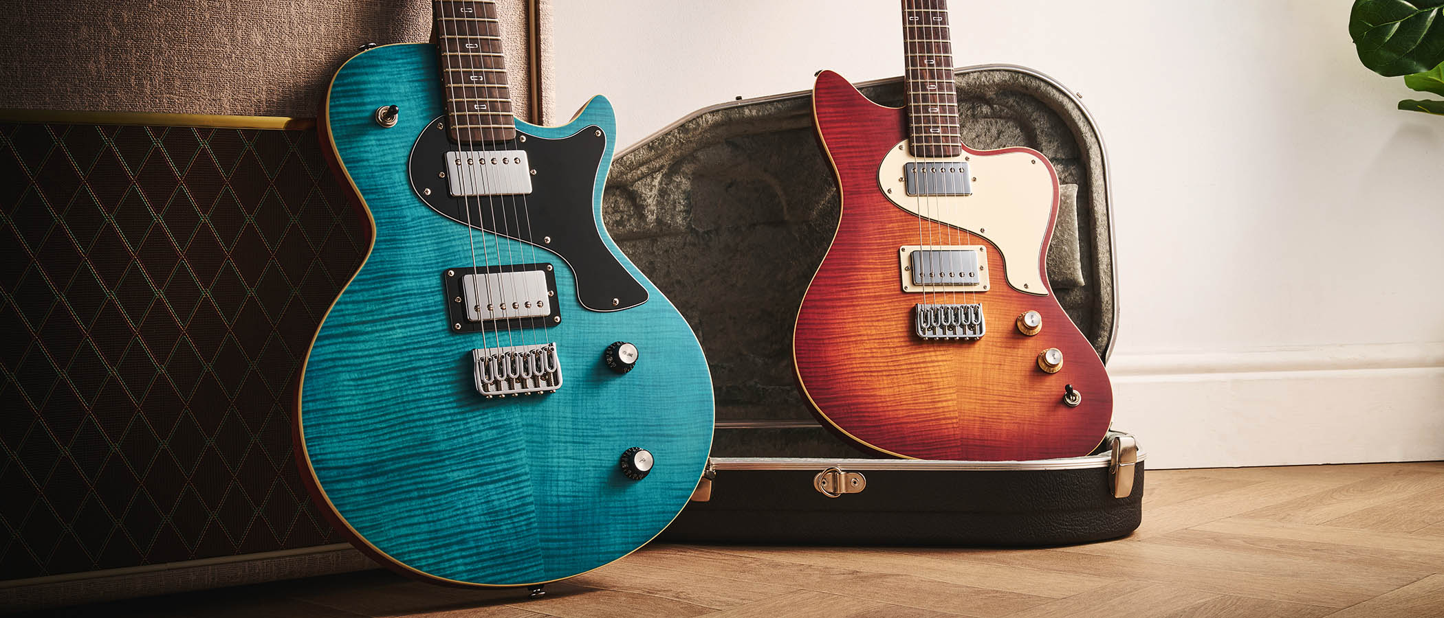 PJD Origin Series Carey Pro and PJD Origin Series St John Pro: the Sea Blue and Original Burst electric guitars are photographed against a fawn-coloured Vox amp with the offset resting on top of its case.
