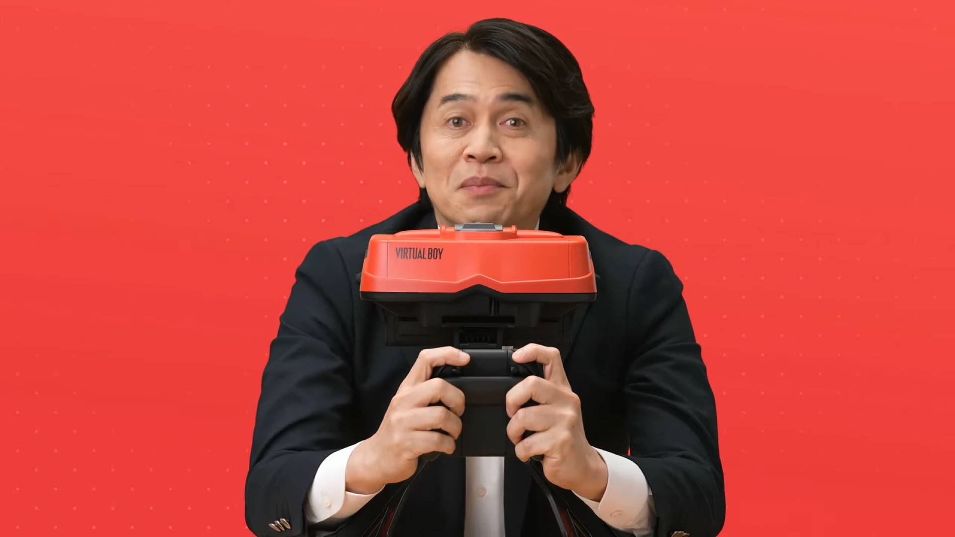 Yoshiaki Koizumi holding Virtual Boy for Switch 2 with red backdrop