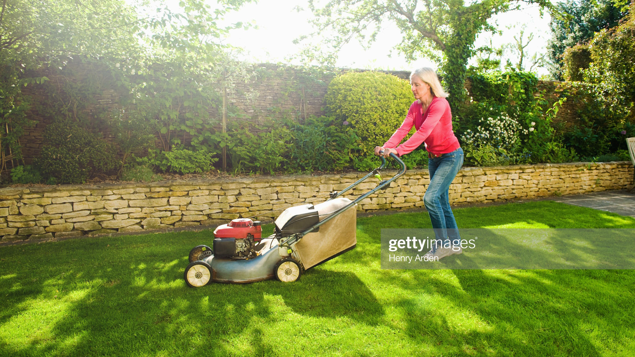 Best gas lawn mowers: A mature woman wearing a red top users a gas lawn mower to cut the grass on a sunny day