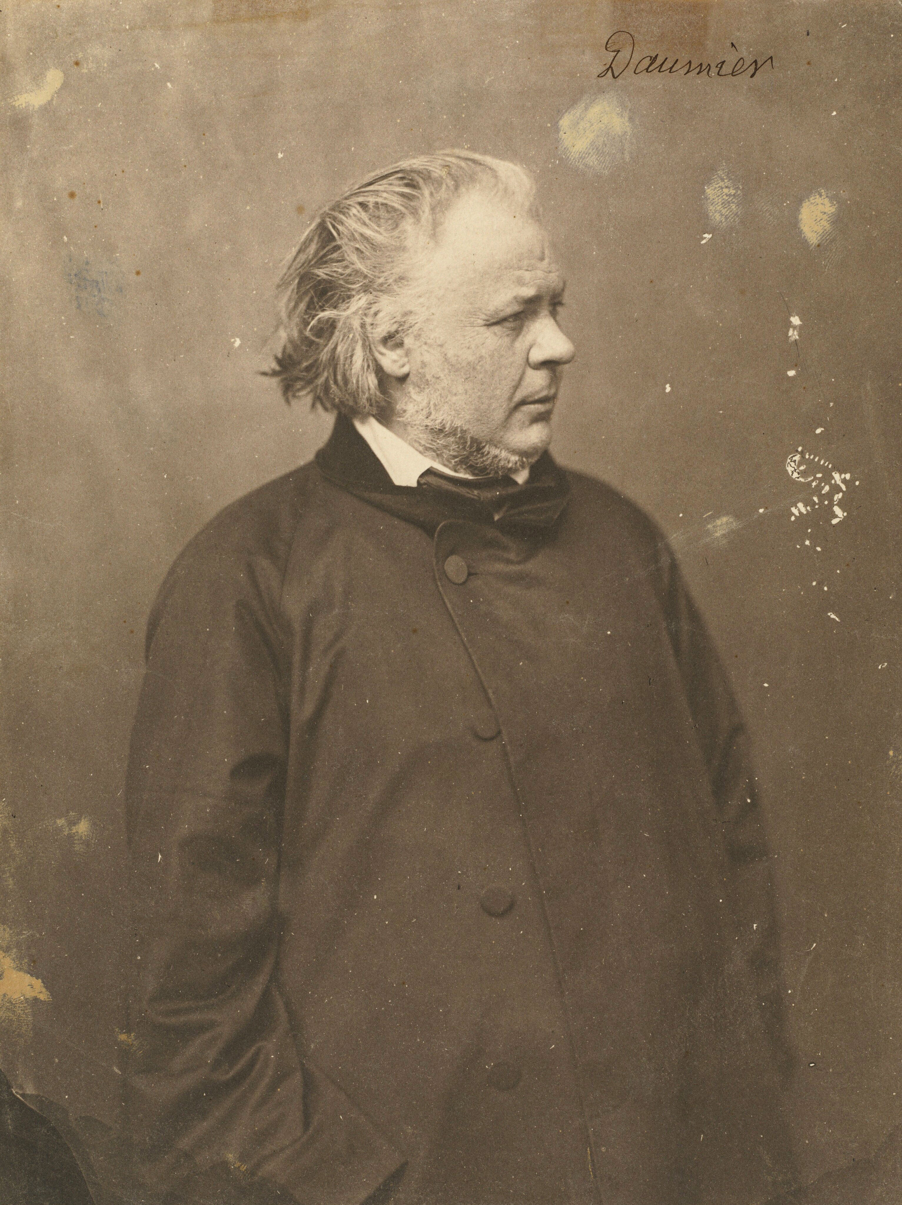 A historic sepia portrait photograph showing the French painter and caricaturist Honor&amp;eacute; Daumier in a dark overcoat, captured in profile looking toward the right.