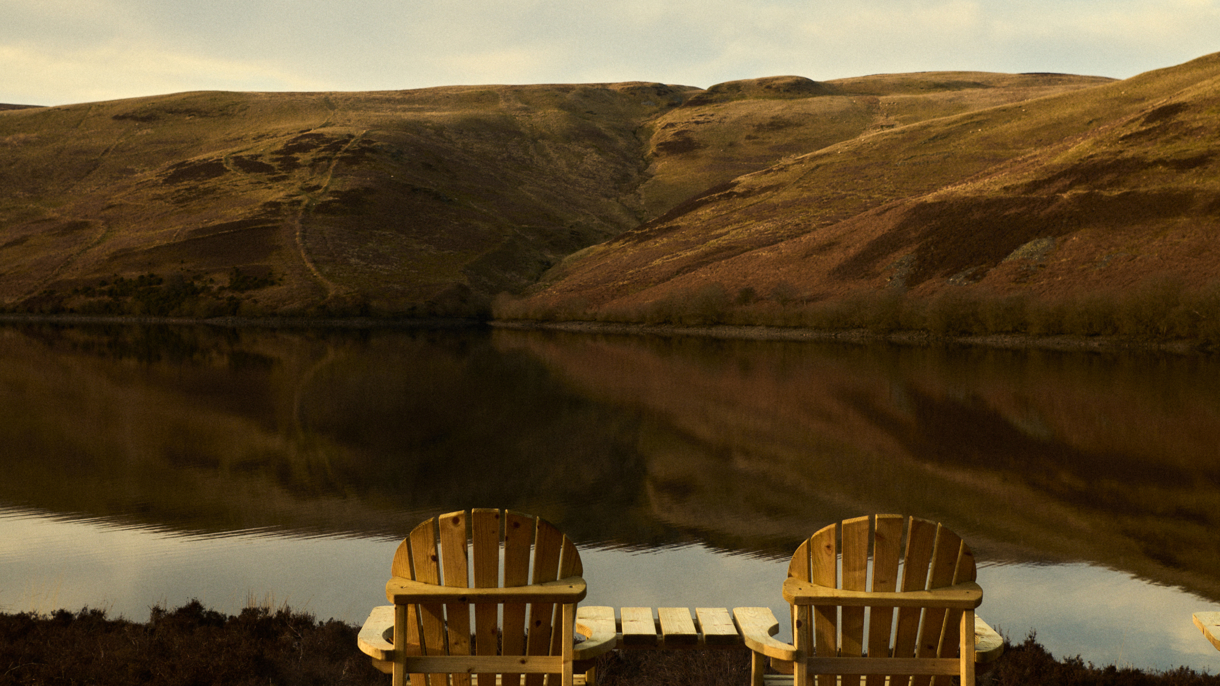 Two wooden deck chairs overlooking a Scottish lake