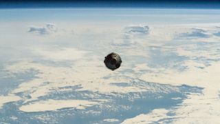 A metallic capsule is seen, looking very tiny against the backdrop of Earth.