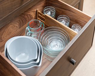 Wooden kitchen island drawer with vertical divider, contains nesting bowls, jugs and glassware