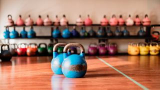 Two kettlebells on gym floor, rack of kettlebells in background