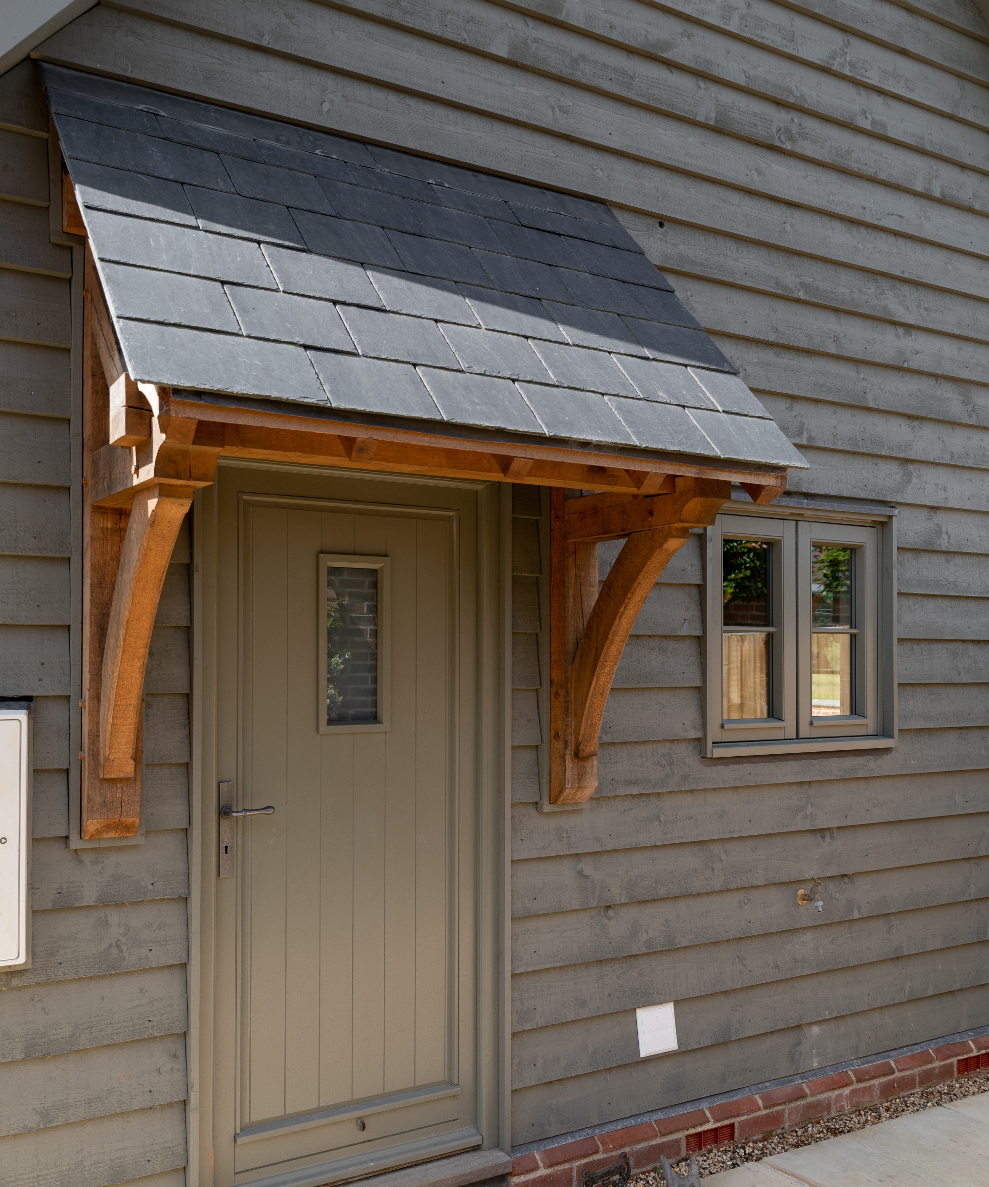 oak frame canopy with black slate roof on house with soft grey/green timber cladding and pale green door