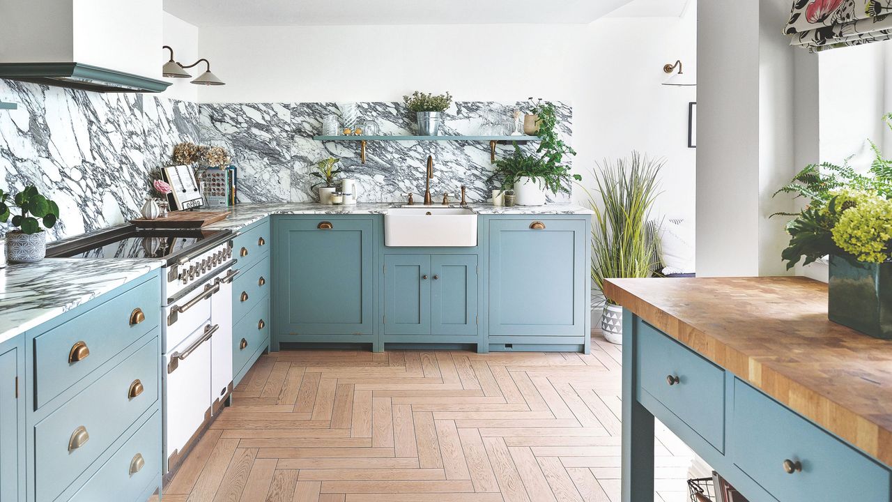 White kitchen with wooden flooring and blue cabinets, with marble on the counters and splashback