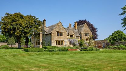 A stone house with manicured lawn and vegetation surrounding