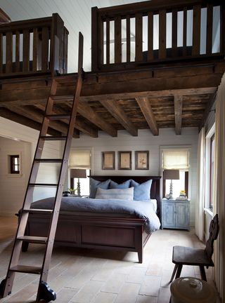 bedroom with blue linen and pale stone floor paneled walls and dark wood mezzanine with wood ladder up