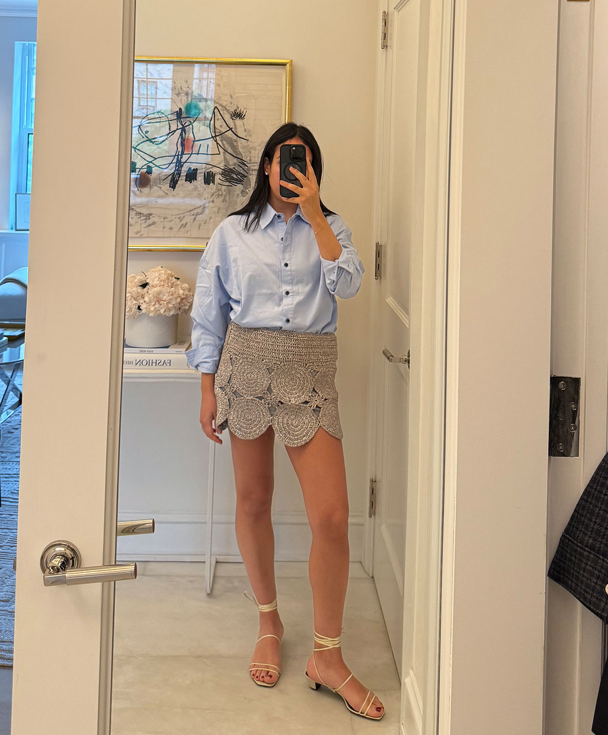 @nicoleakhtarzad taking a mirror outfit selfie and wearing a button down shirt and crochet mini skirt.