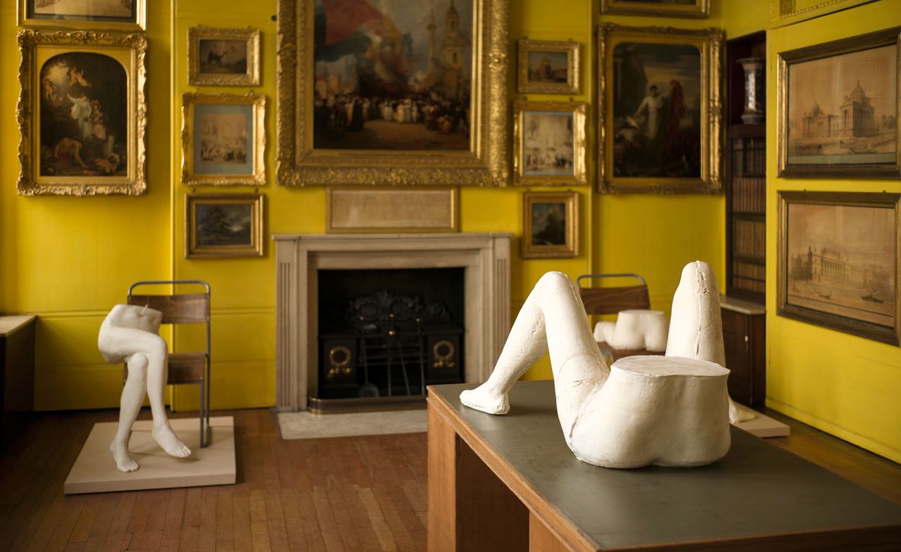 Sculptures of female legs with golden framed images on wall