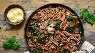 Bowl of wholewheat pasta with scattering of cheese and some green vegetables