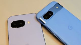 The Iris Google Pixel 9a (left) and Bay Google Pixel 8a (right), the 8a slightly overlapping the 9a corner. The photo focuses on the 9a's new camera cutout compared to the 8a's camera bar.