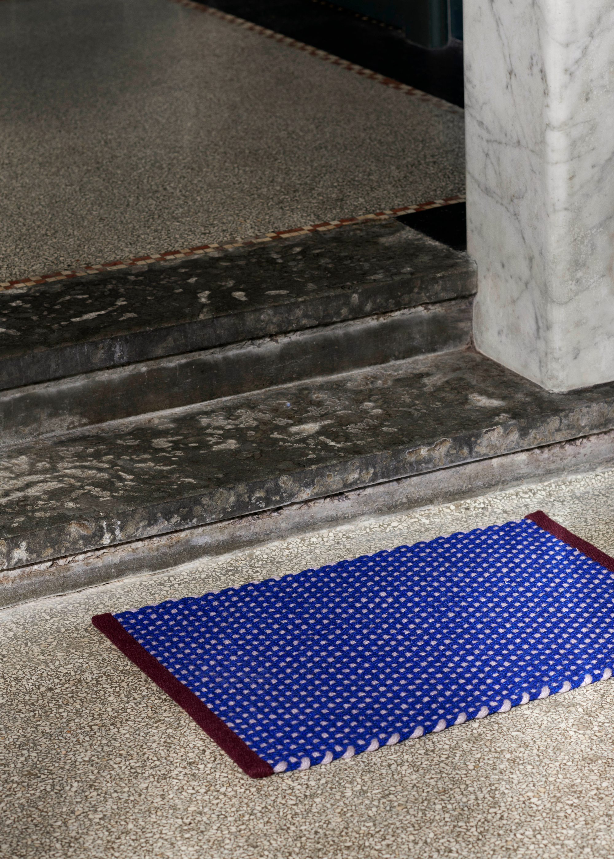 A close-up of stone steps by a bright cobalt blue doormat with burgundy hemming